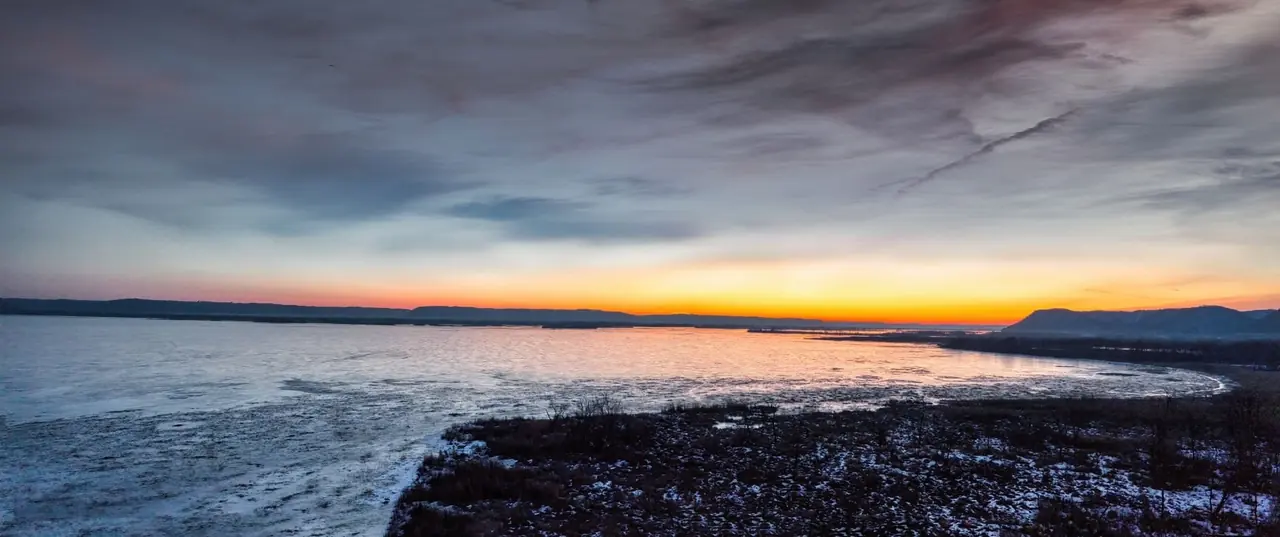 Fleuve pris par la glace au coucher du soleil, bande orange sous un ciel chargé