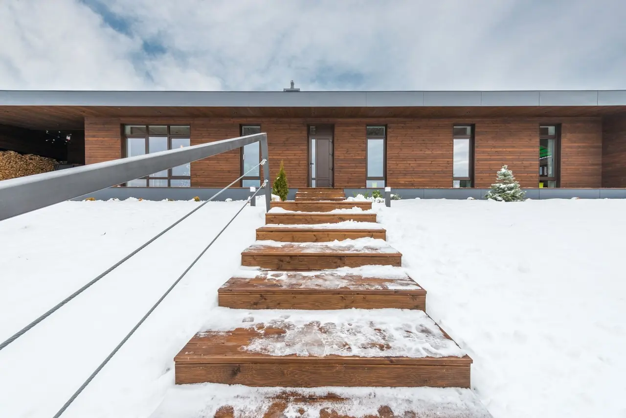 Marches de bois dans la neige menant à une maison moderne revêtue de bois