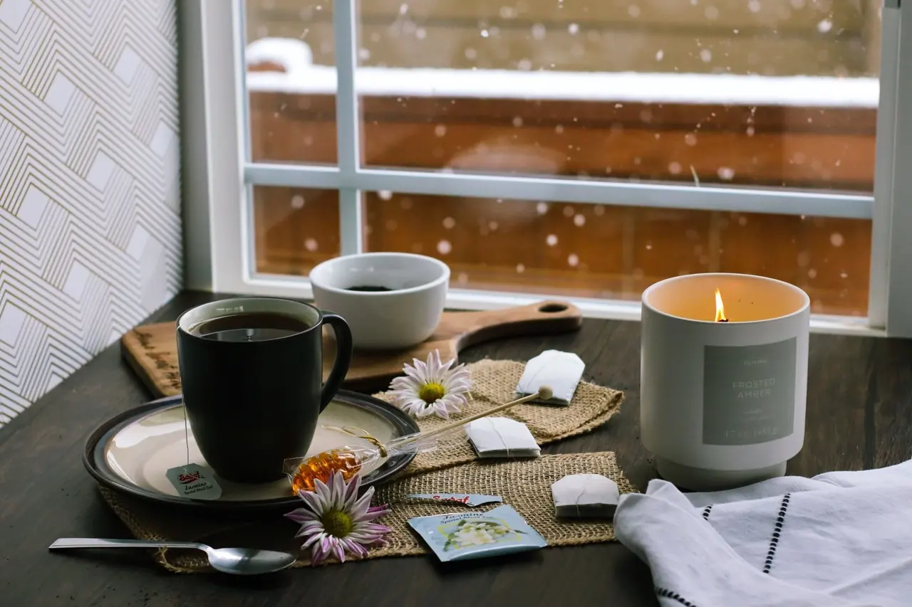 Tasse de café et bougie allumée sur une table devant une fenêtre où il neige