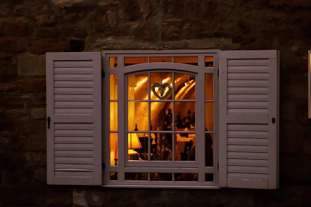 Fenêtre à volets éclairée d'une lumière chaude dans un mur de pierre sombre