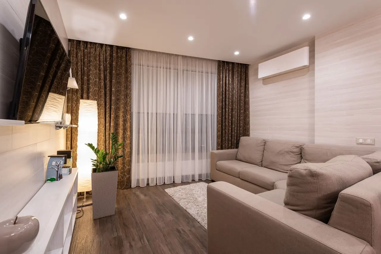Salon beige avec thermopompe murale au-dessus du canapé et rideaux sombres