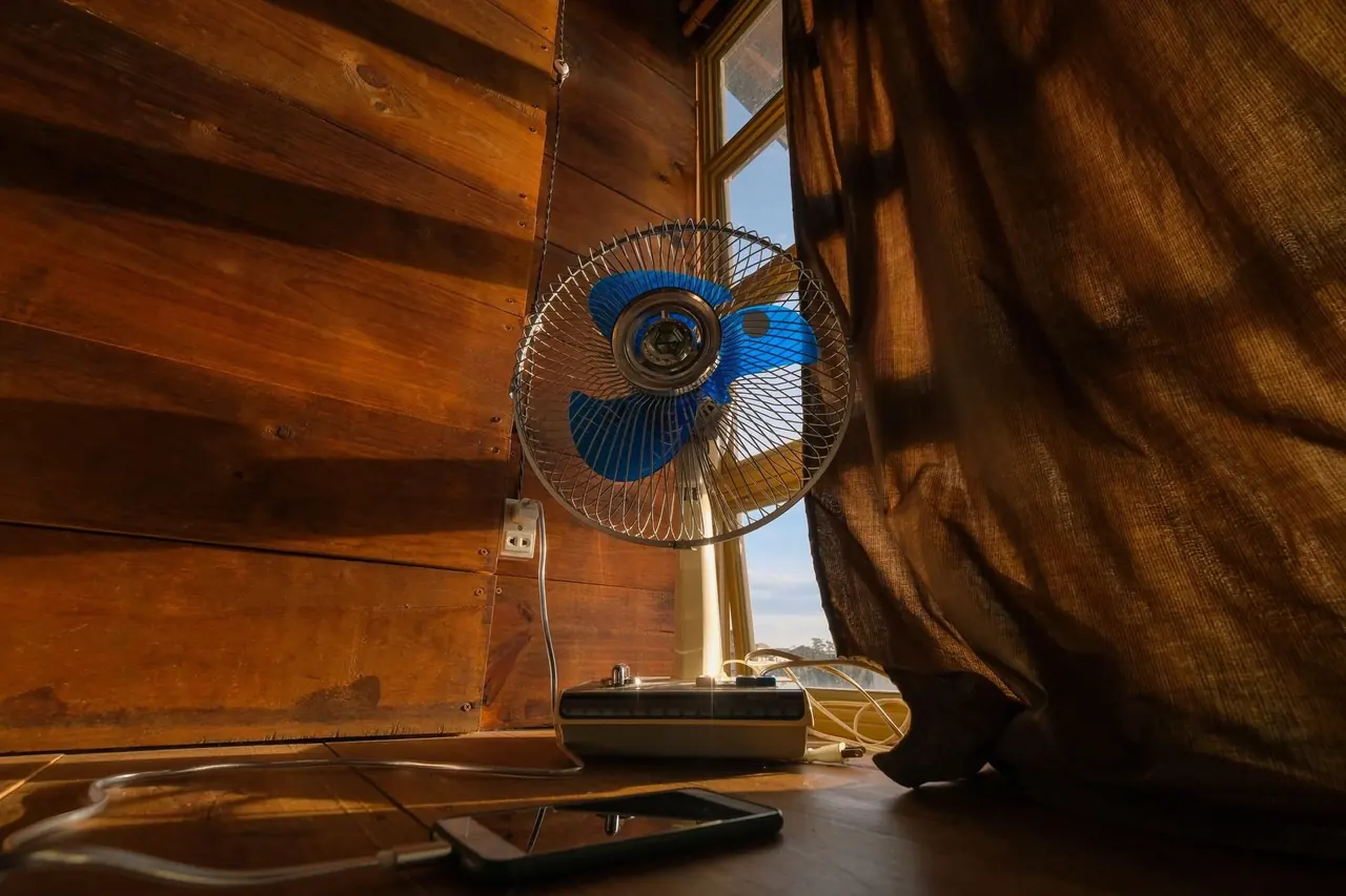 Petit ventilateur sur un rebord de bois près d'un rideau de lin soufflé par l'air