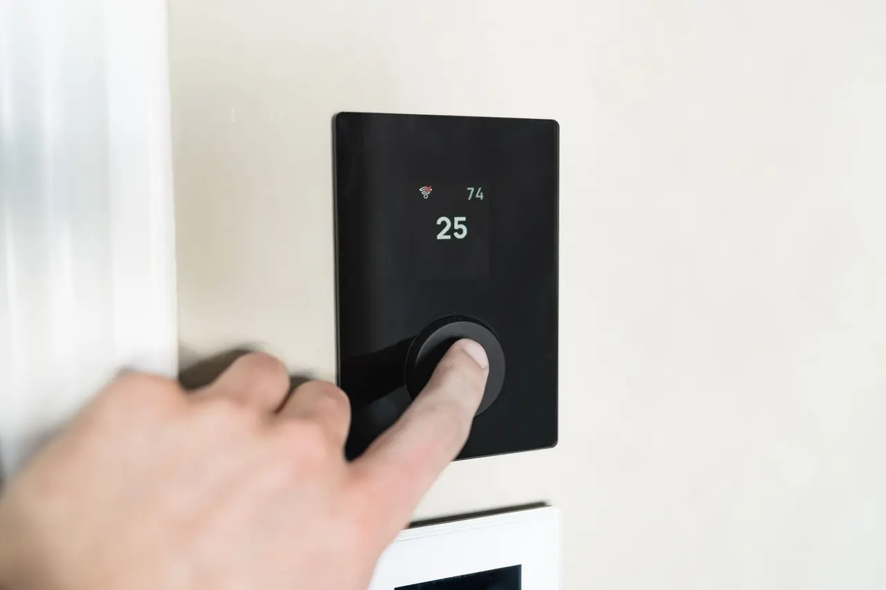 Doigt sur un thermostat noir à molette indiquant 25