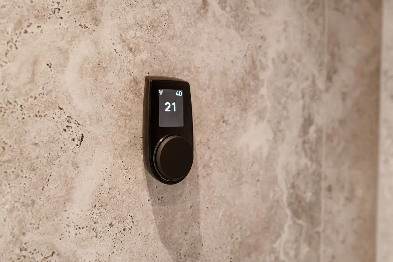 Thermostat numérique noir indiquant 21 sur un mur de pierre beige