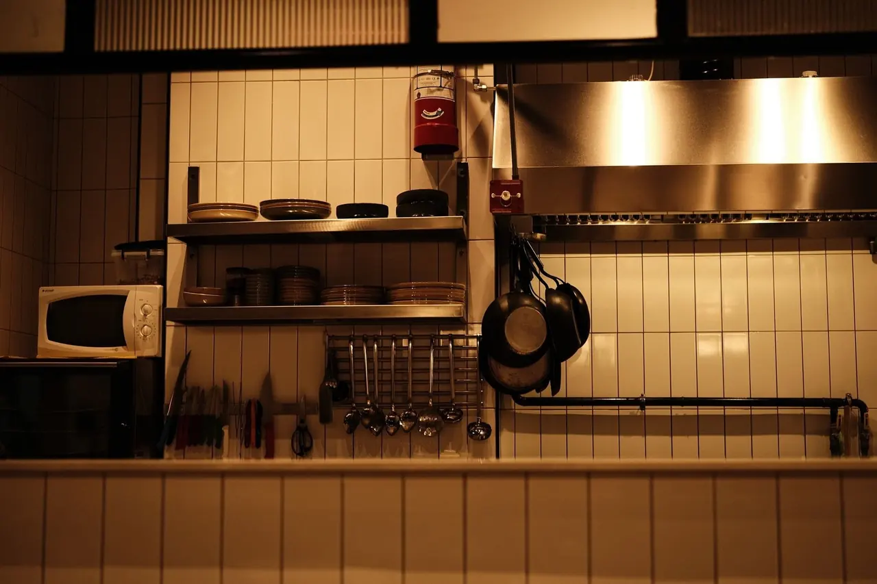 Cuisine professionnelle avec hotte en inox, carrelage blanc et poêles suspendues