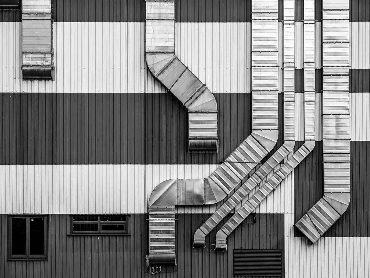 Conduits de ventilation galvanisés le long d'une façade industrielle, en noir et blanc