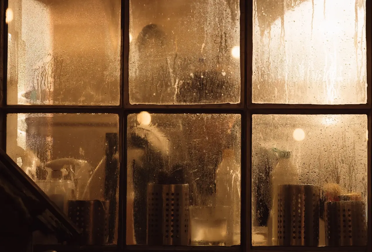 Fenêtre à carreaux embuée, éclairée d'une lumière chaude, un soir d'hiver