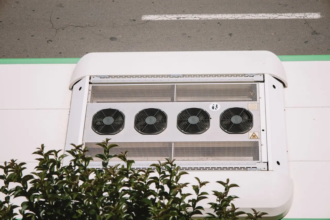 Unité de climatisation blanche à quatre ventilateurs derrière des arbustes verts